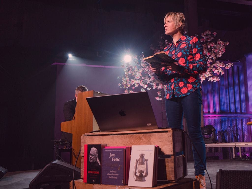 Foto av Linda Eide på scenen som leser fra en bok.